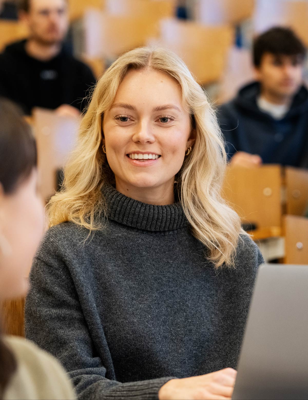 En student smiler mot kamera i en forelesningssal