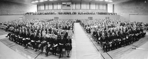 Mange festkledde mennesker sitter i stor hall og venter på immatrikuleringsseremoni