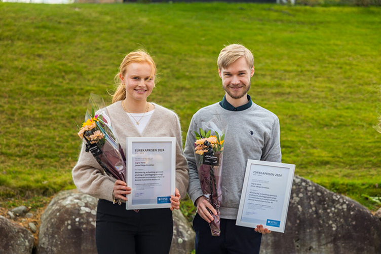 To studenter står ute med priser og blomster. Foto