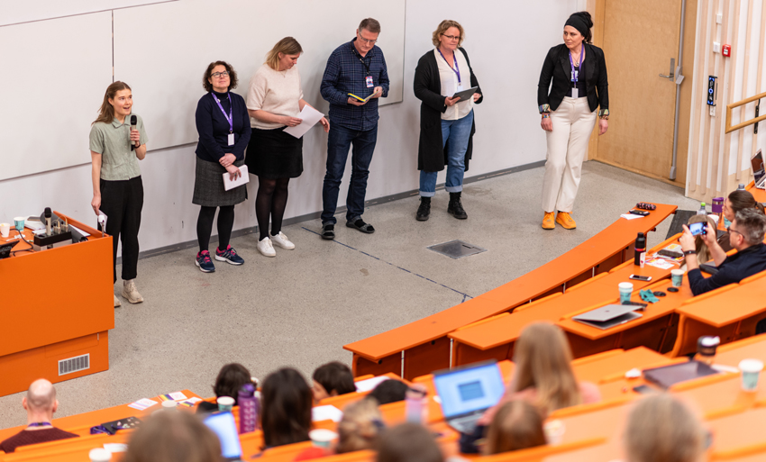 Seks personer står og presenterer på en konferanse. Foto