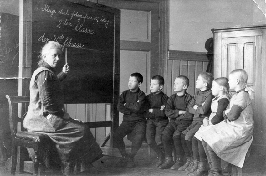 En gruppe elever på døveskolen som sitter ved en tavle sammen med en lærer som peker på tavlen.