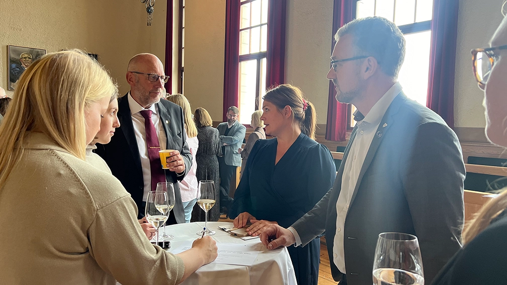 Fem personer som står rundt et bord og snakker, rektor i midten. Foto: NTNU