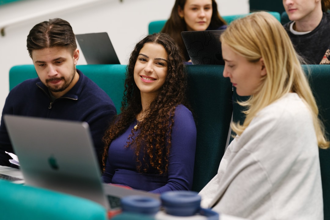 Studenter sitter i et auditorie. Hun i midten ser i kamera. 