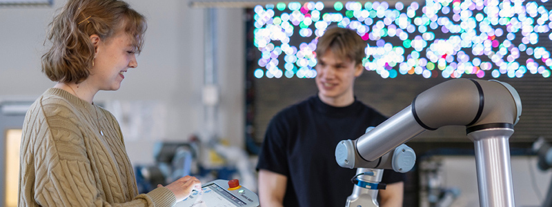 Bilde av to studenter som samarbeider med en robot. 