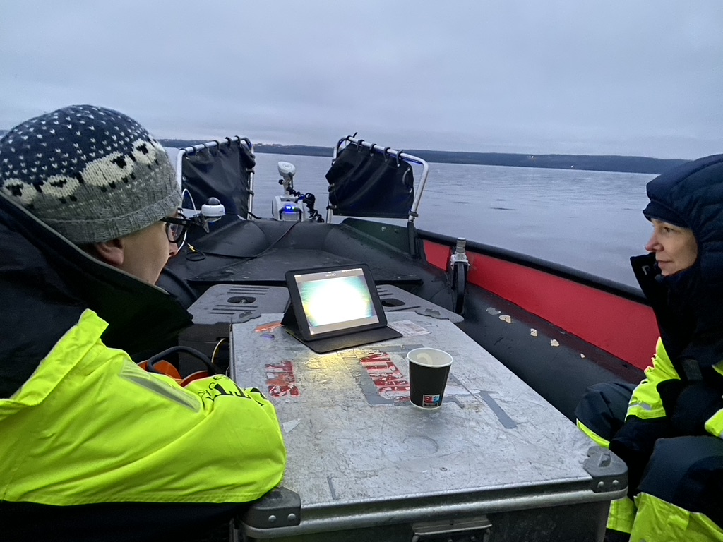 To personer ser på et kart og er ute i en båt på Mjøsa