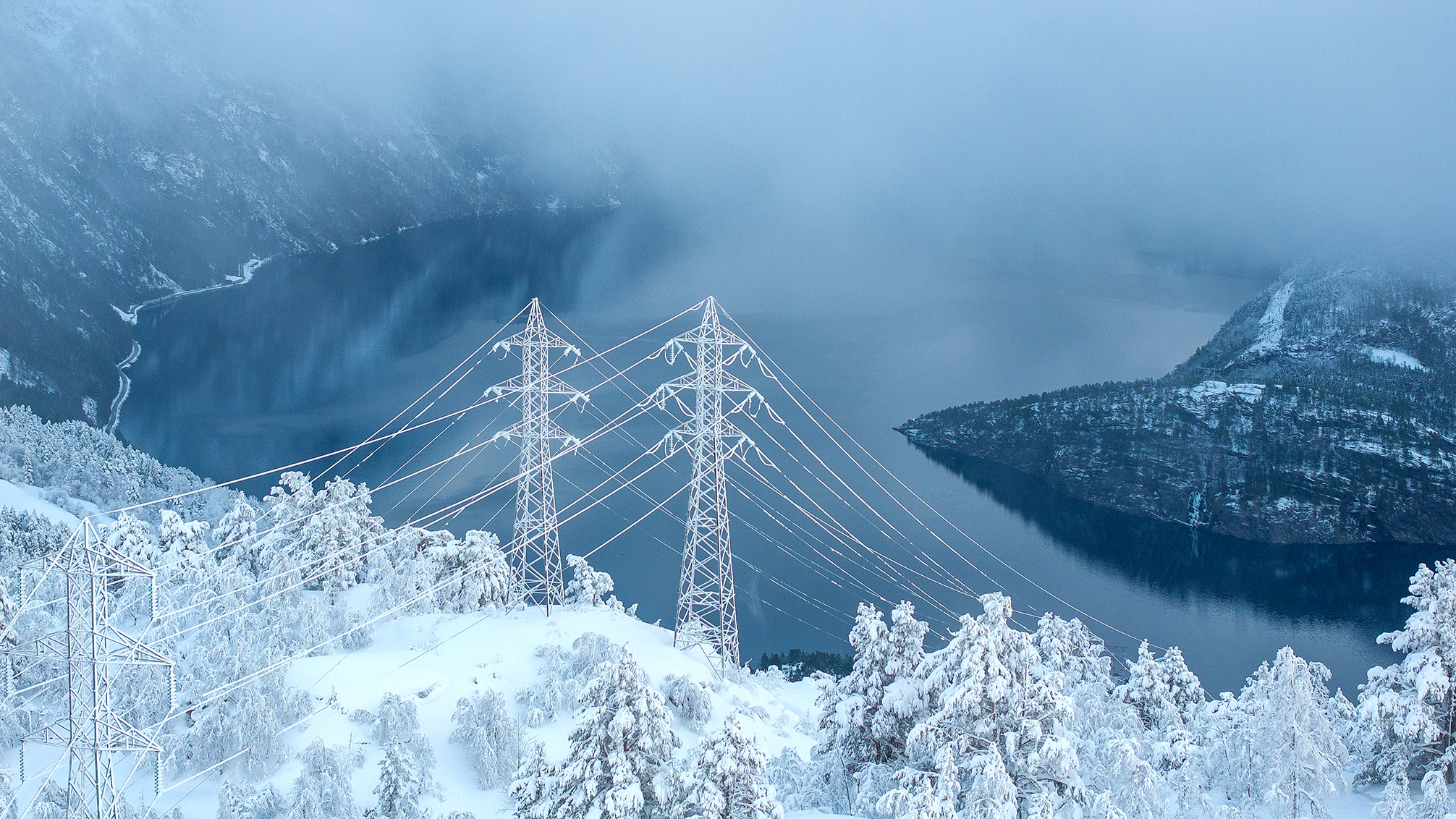 Høystpentledninger over en fjord i et fjellterreng med snø. Foto