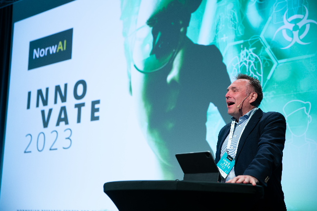 En person presenterer ved et podium med ‘NorwAI INNOVATE 2023’ på skjermen