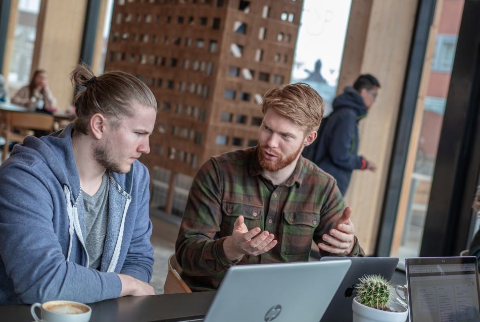 To mannelige studenter diskuterer over en pc. Mjøstårnet i bakgrunn.