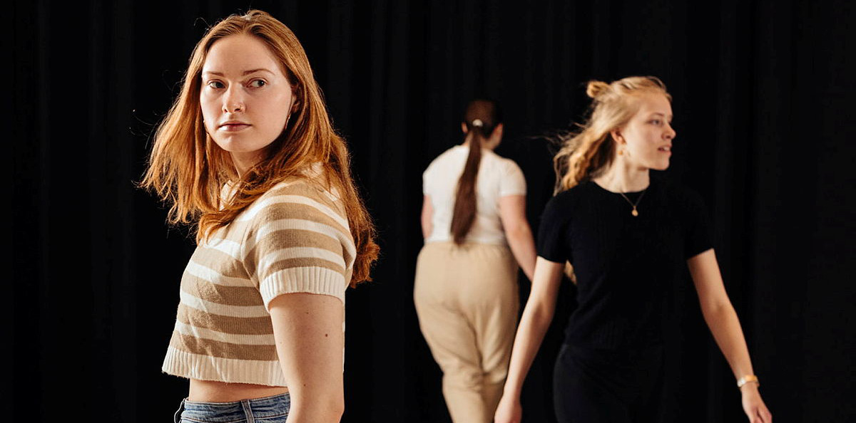 A photo of a student theater production where three young female studentswalk in different directions.