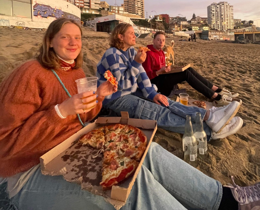 Studenter sitter på stranden og spiser pizza. Foto