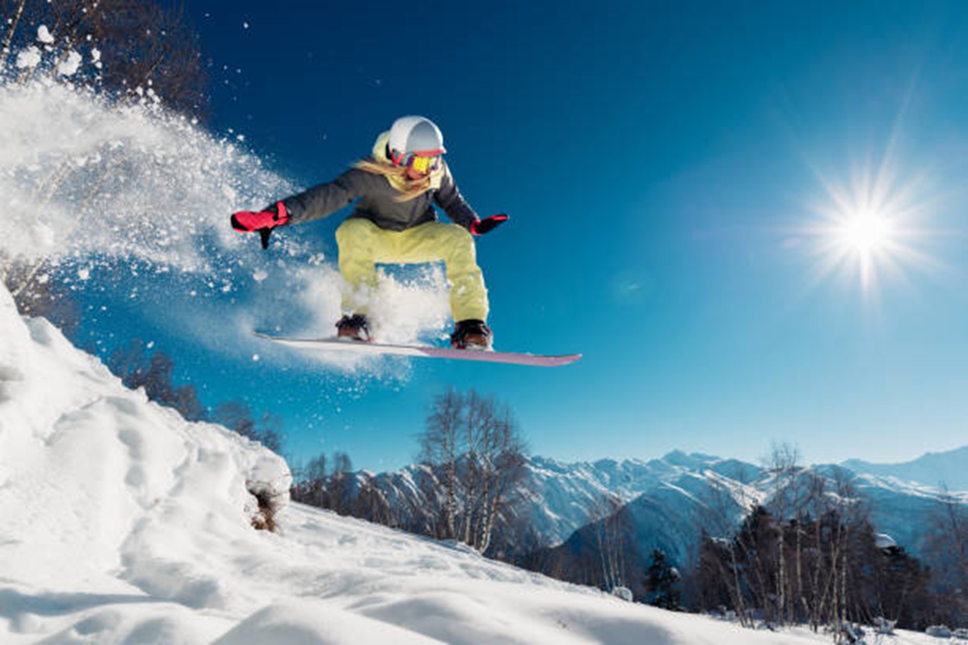 En person som står på snowboard med sol i bakgrunnen. Foto.