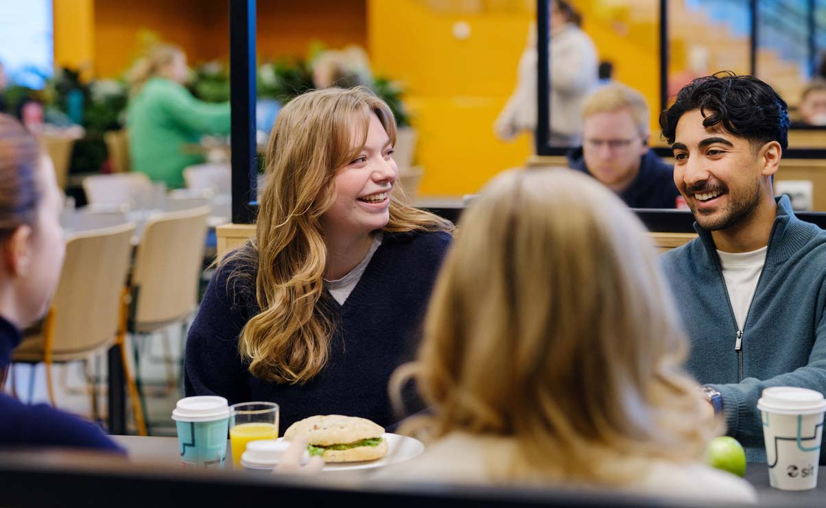 Studenter på kafé, ler og ser på hverandre.